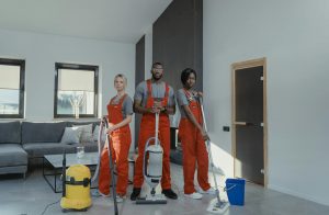Diverse commercial cleaning services team in red uniforms ready to sanitize a modern living room with vacuum and mop.